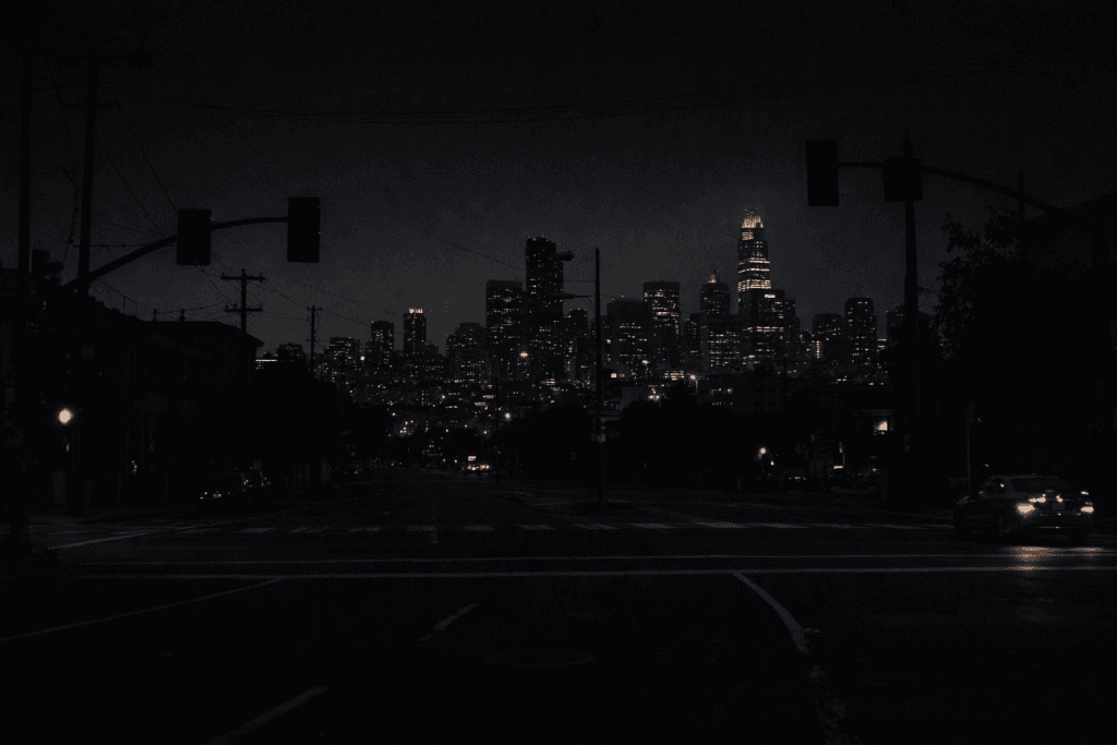 Dark San Francisco intersection during a citywide power outage, with unlit traffic signals and the downtown skyline dimly visible at night.